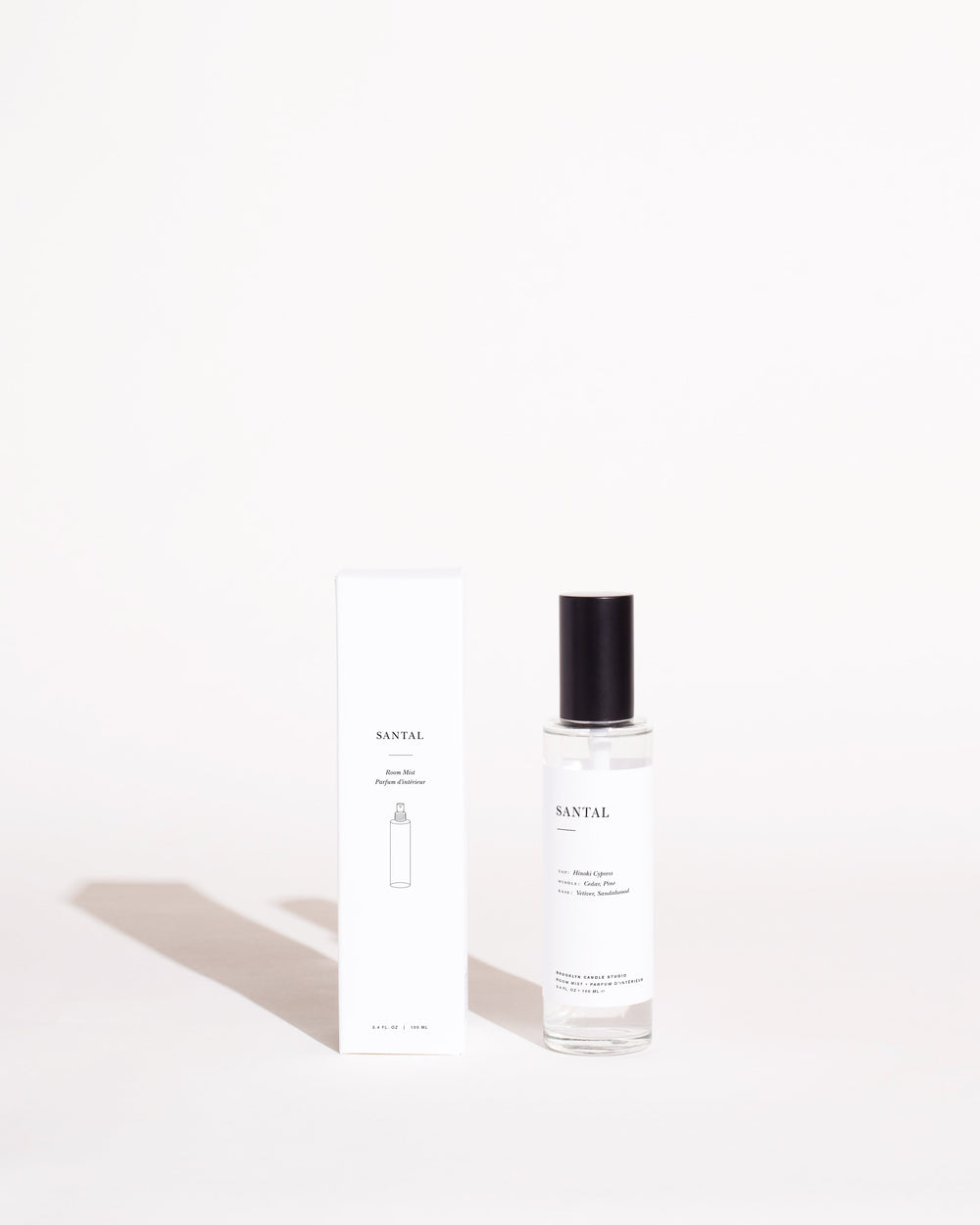 A bottle of Santal Room Mist, featuring a black cap, next to a white box. Earthy scent of Hinoki Cypress, cedar, pine, vetiver, and sandalwood. Vegan, paraben-free, cruelty-free.